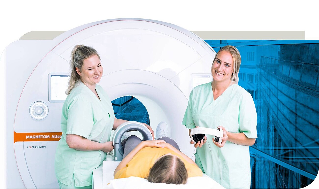 Zwei medizinische Fachkräfte in grüner Arbeitskleidung bereiten eine Patientin für eine MRT-Untersuchung vor. Die Patientin liegt auf dem Untersuchungstisch vor einem MRT-Gerät, während die Fachkräfte lächeln und ein Headset bereithalten. Der Hintergrund zeigt eine blau eingefärbte Krankenhausumgebung