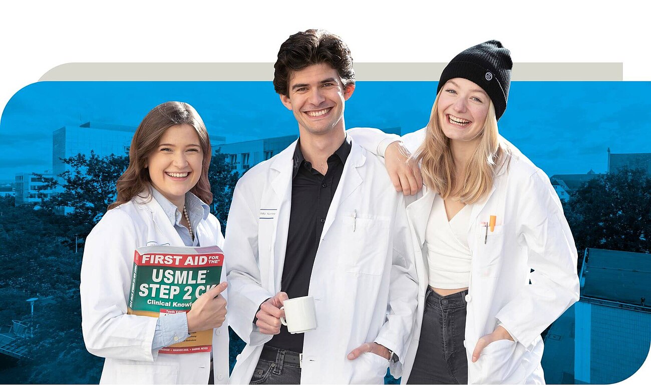 Drei Medizinstudierende in weißen Kitteln stehen lachend zusammen. Eine Frau hält ein Lehrbuch mit der Aufschrift ‚First Aid for the USMLE Step 2 CK‘, ein Mann hat eine Tasse in der Hand, und eine andere Frau trägt eine schwarze Mütze und lächelt herzlich