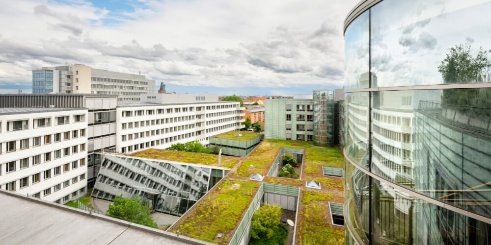 Blick von oben auf einen begrünten Innenhof, umgeben von modernen Gebäuden mit großen Glasfassaden. Die Architektur ist offen gestaltet, mit viel Grün auf den Dächern und in den Höfen.