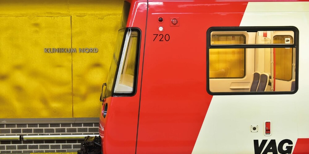 Eine goldene U-Bahn-Station mit der Aufschrift „Klinikum Nord“ an der Wand. Im Vordergrund steht ein rot-weißer Zug der VAG Nürnberg, dessen Fenster und Sitzplätze sichtbar sind