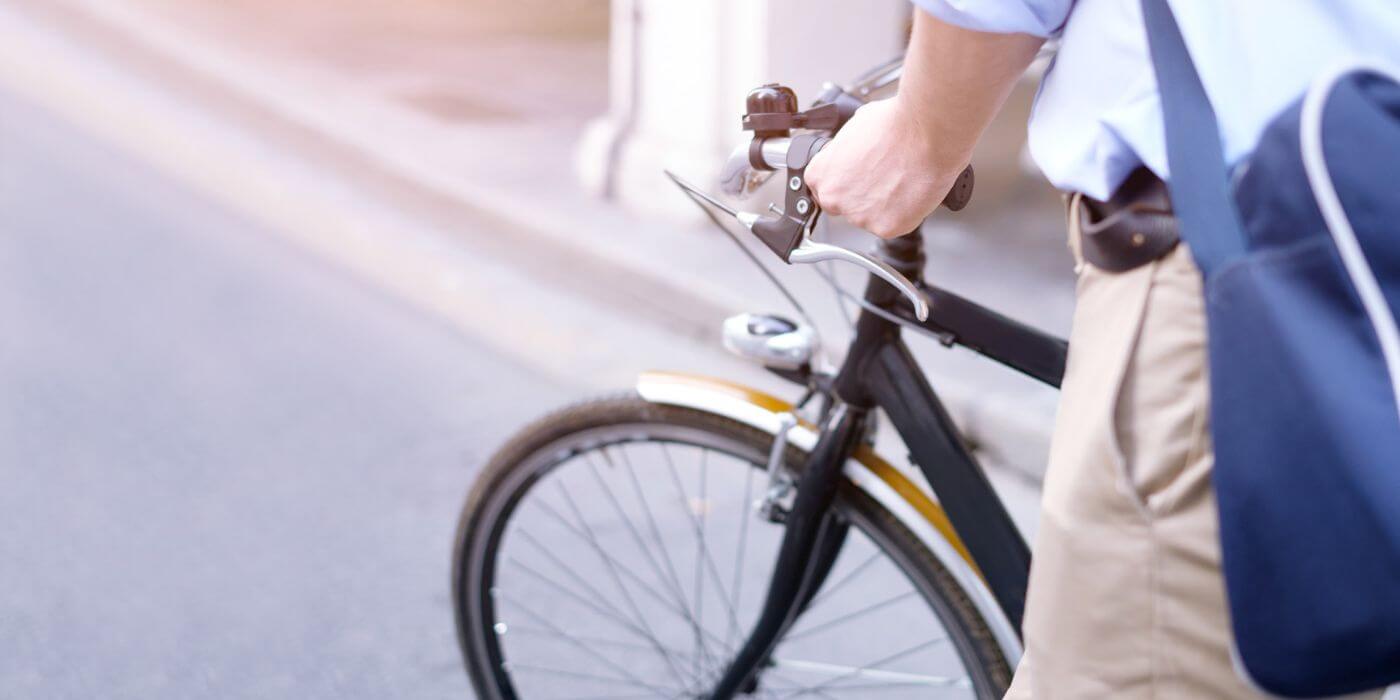 Nahaufnahme eines Mannes, der ein Fahrrad schiebt. Das Bild symbolisiert die Möglichkeit des Fahrradleasings als Mitarbeiter-Benefit