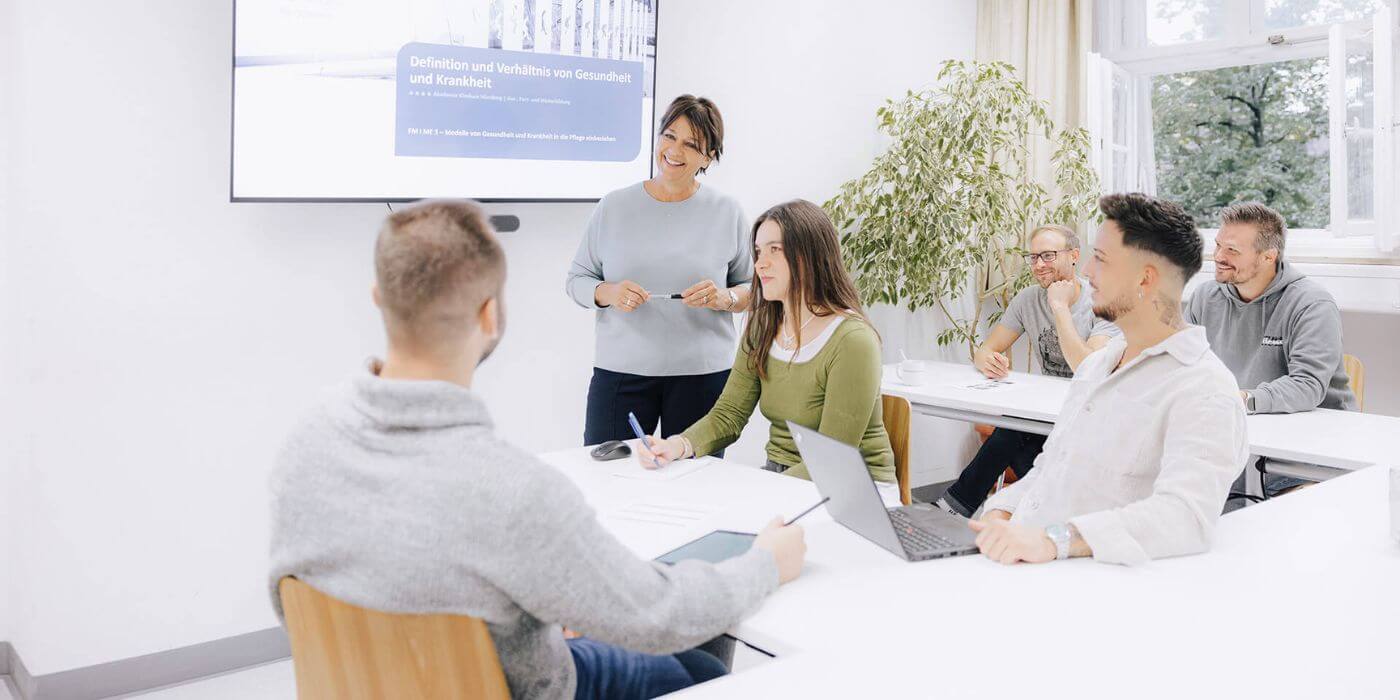 Drei Personen in einem modernen Seminarraum, während eine Frau eine Präsentation hält. Das Bild repräsentiert Fort- und Weiterbildungsmöglichkeiten