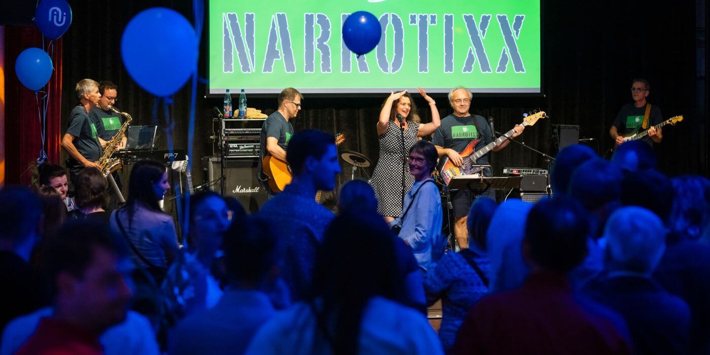 Die Band Narkotixx spielt auf einer Bühne vor einem Publikum. Menschen im Vordergrund tanzen und genießen die Veranstaltung