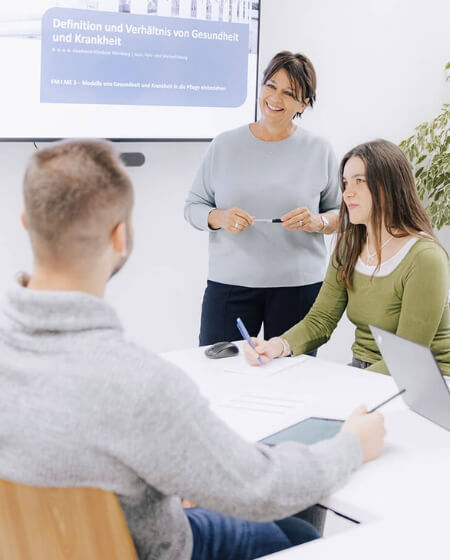 Drei Personen in einem modernen Seminarraum, während eine Frau eine Präsentation hält. Das Bild repräsentiert Fort- und Weiterbildungsmöglichkeiten