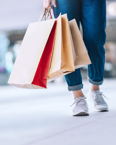 Eine Person in Sneakers trägt mehrere Einkaufstüten in verschiedenen Farben. Das Bild symbolisiert Vorteile wie Mitarbeiterrabatte oder andere Benefits