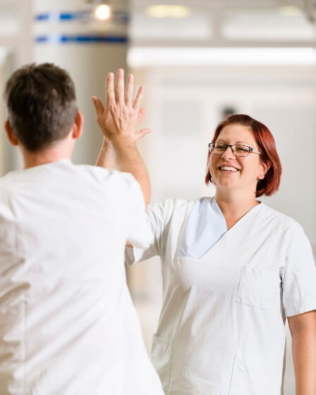 Zwei Pflegefachkräfte in weißen Kitteln geben sich lächelnd ein High-Five in einer hellen, modernen Umgebung