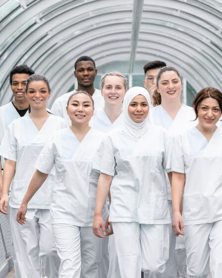 Eine Gruppe von medizinischem Fachpersonal in weißen Kitteln geht gemeinsam durch einen hellen, überdachten Gang. Das Bild vermittelt Teamgeist und Zusammenarbeit im Gesundheitswesen