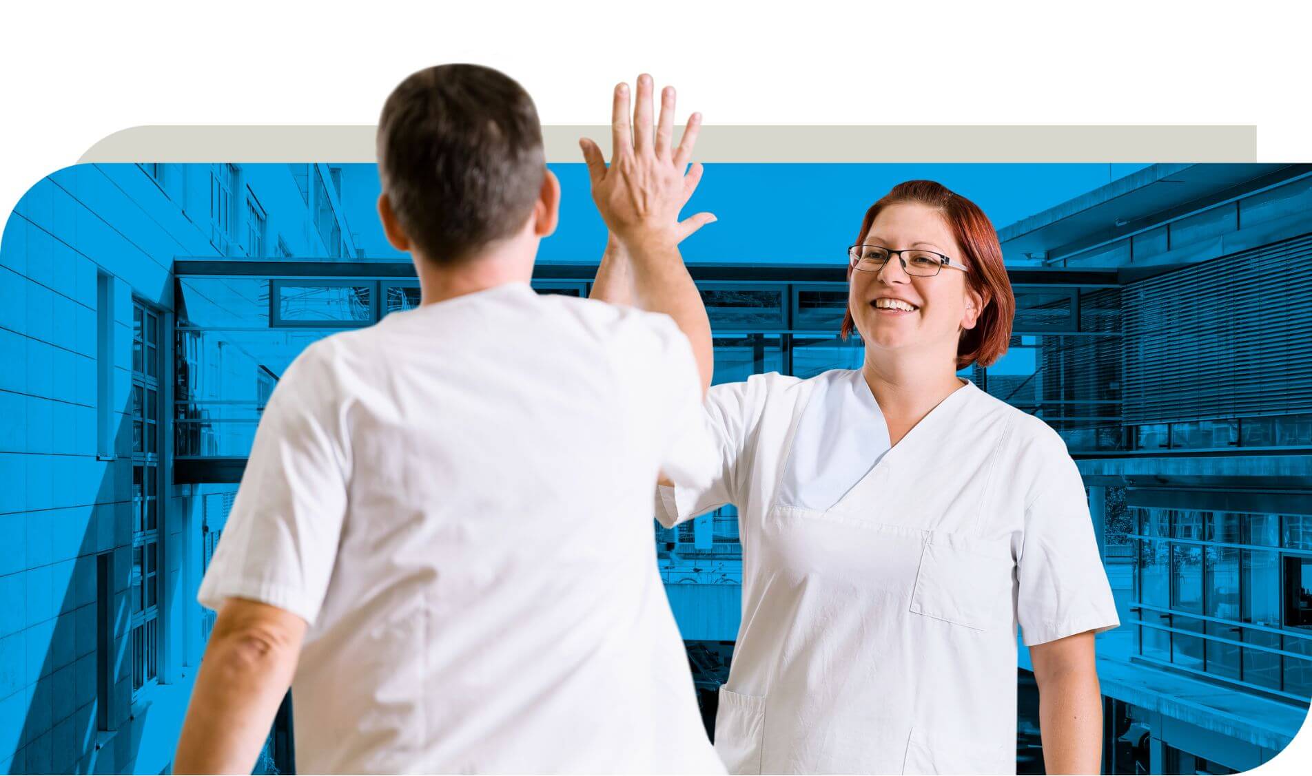 Zwei Pflegekräfte in weißer Arbeitskleidung geben sich ein High-Five. Im Hintergrund ist eine blau eingefärbte Ansicht eines Krankenhausgebäudes zu sehen. Beide Personen lächeln und wirken motiviert