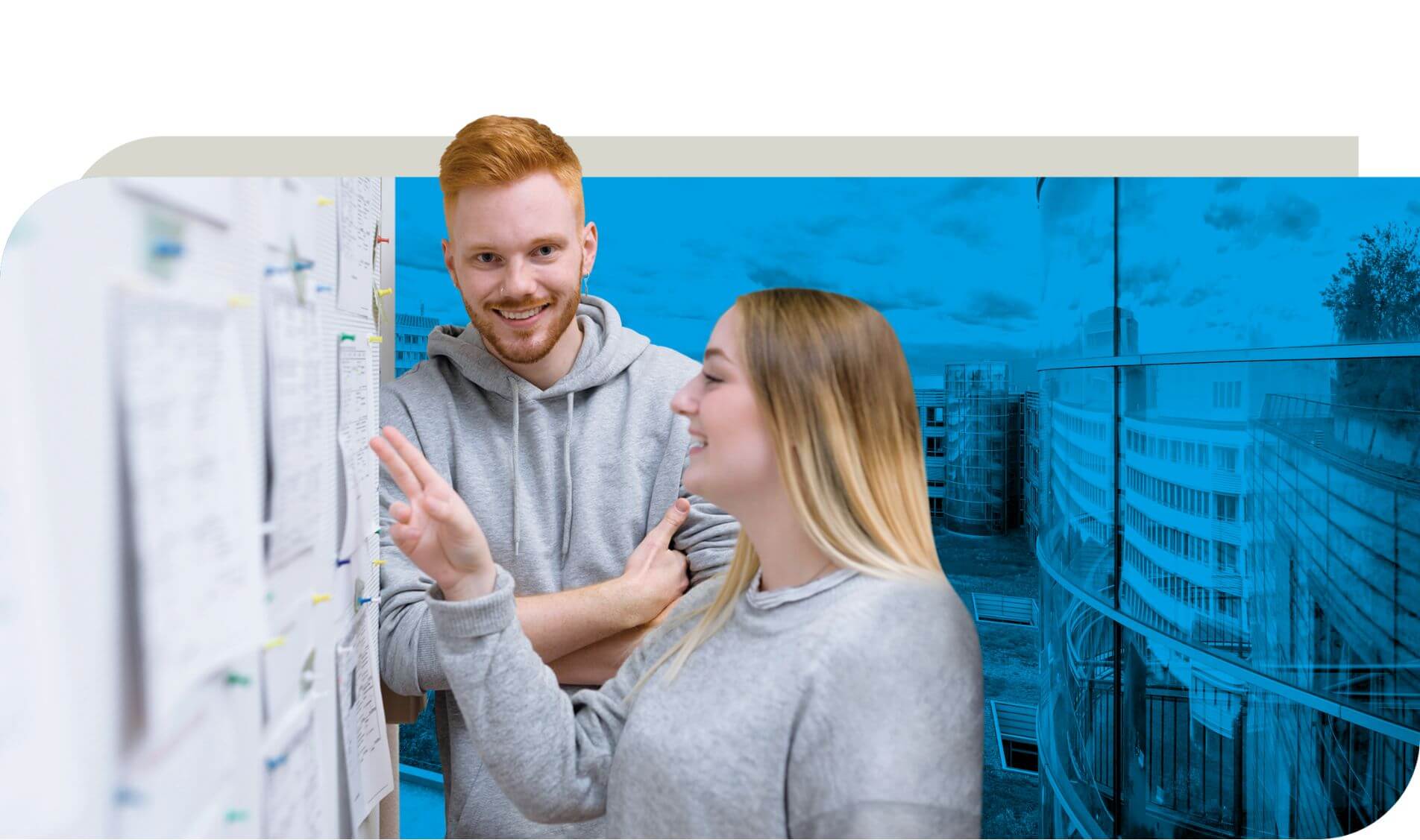 Zwei junge Personen stehen vor einer Pinnwand mit verschiedenen Notizen und Plänen. Eine Person zeigt mit der Hand auf die Wand, während die andere aufmerksam zuhört. Im Hintergrund ist ein modernes Gebäude zu sehen