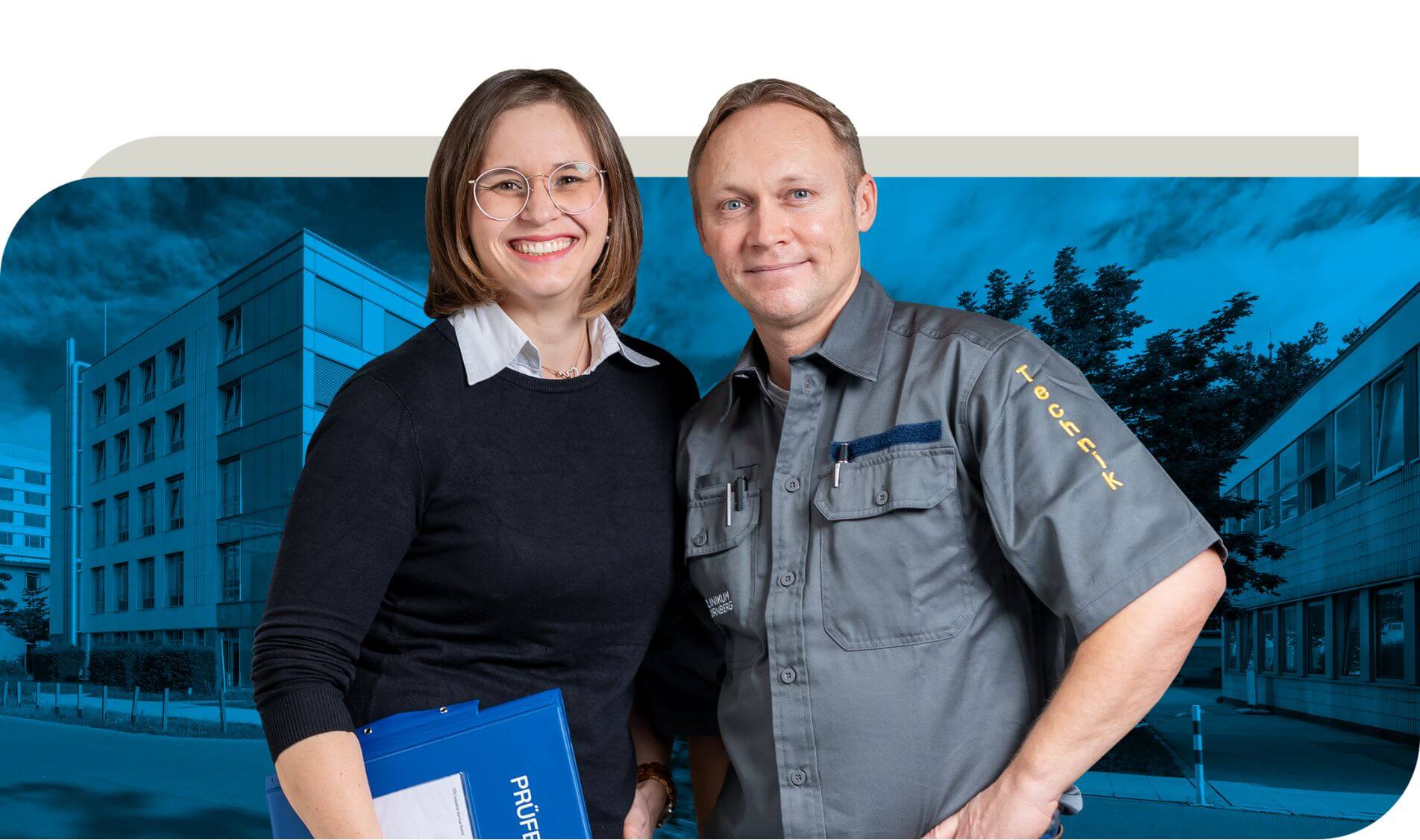 Ein Mitarbeiter in grauer Arbeitskleidung mit der Aufschrift "Technik" steht neben einer Kollegin in schwarzer Kleidung, die einen blauen Ordner hält. Beide stehen vor einem modernen Gebäude.